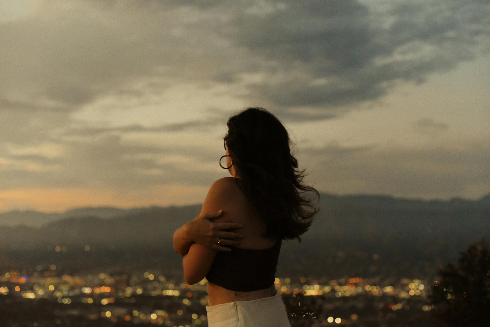 A woman embraces the serene sunset over Los Angeles, blending nature with city lights.