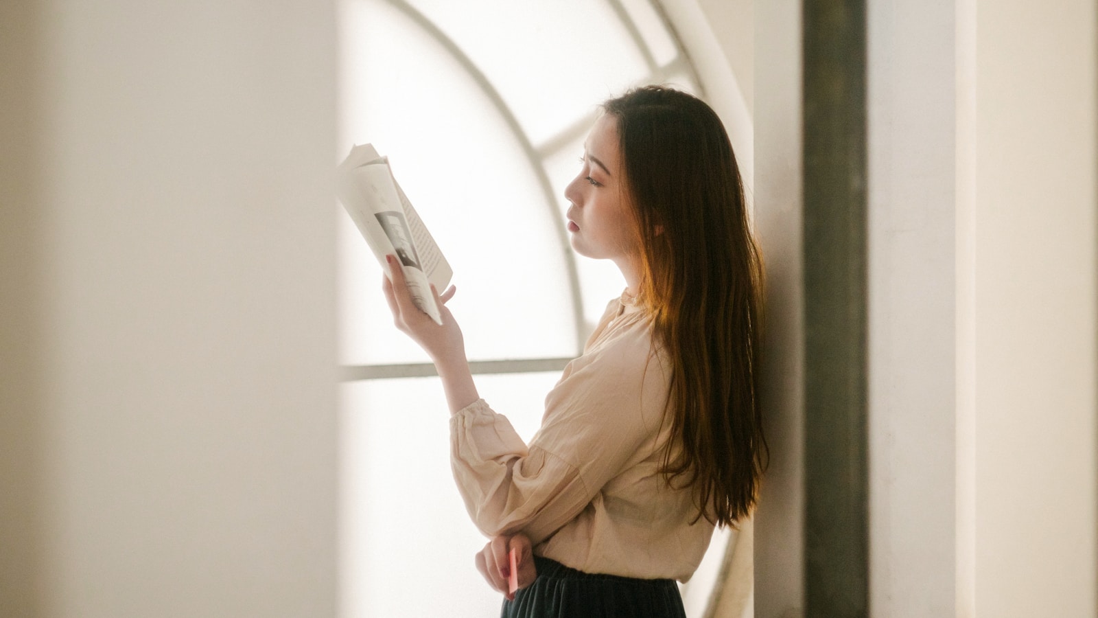 woman leaning on the wall while reading book